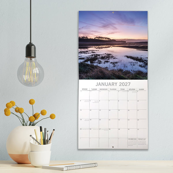 Devon Calendar for January 2027 on a wall with decorative items below.
