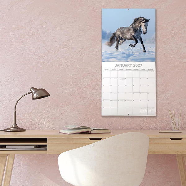 Wall calendar with a horse on a pink wall above a desk.