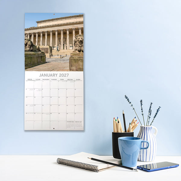 Liverpool Calendar with January 2027 layout on a wall next to a desk with stationery items.