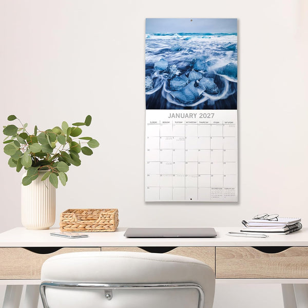 Calendar on a wall above a desk with office supplies and decor.