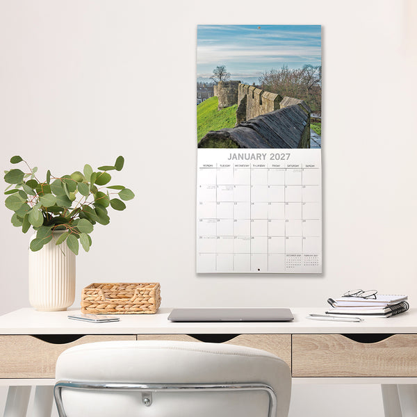 2027 York Calendar on a wall above a desk with a decorative plant and stationery items.