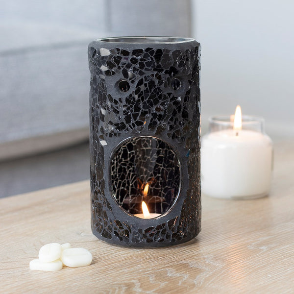 Black textured candle holder with a lit candle inside on a wooden surface.