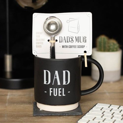 Black mug with 'Dad Fuel' text, coffee scoop, and coaster on a desk.
