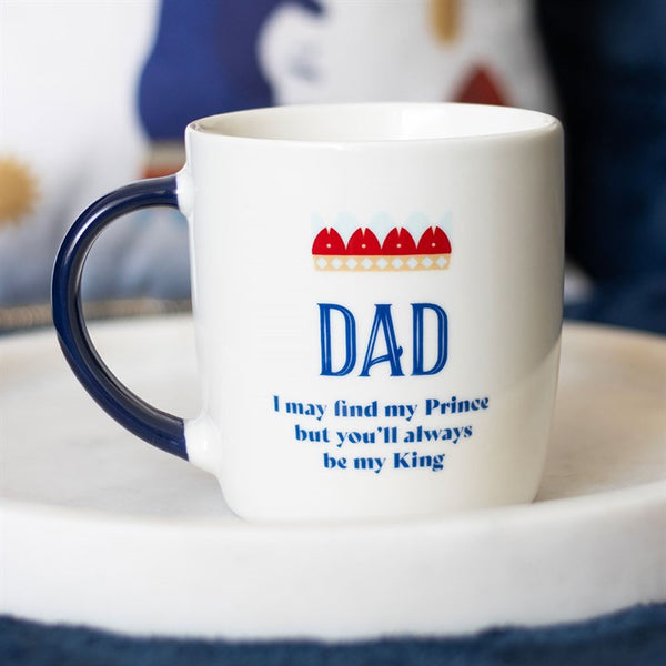 A white ceramic mug with a navy blue handle and a crown design, featuring the text 'DAD' and 'I may find my Prince but you'll always be my King'.