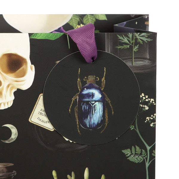 Decorative tag with a beetle design on a black background with skull and plant elements.