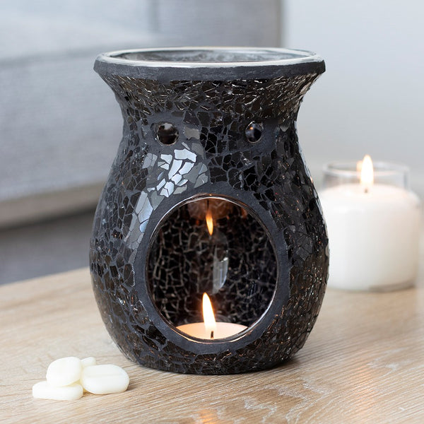 Black mosaic oil burner with a lit candle inside on a wooden surface.