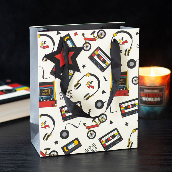 Gift bag with retro design featuring cassette tapes, bikes, and 'Game Over' signs on a dark surface.