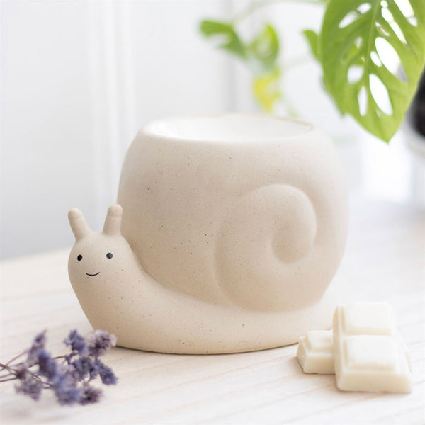 Ceramic snail wax melter on a white surface with a plant and flowers.