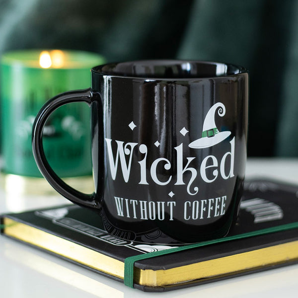 Black mug with 'Wicked Without Coffee' text on a book with a blurred candle in the background